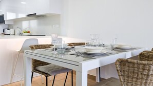 A modern kitchen with white cabinetry, a glass dining table, wicker chairs, and a breakfast bar. - PANORAMIC sweet home (Finestrat)