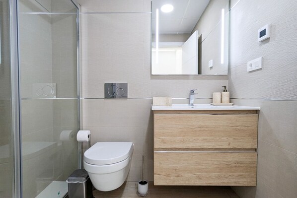 Un baño moderno con cabina de ducha de vidrio, inodoro, tocador de madera con espejo y perchero.