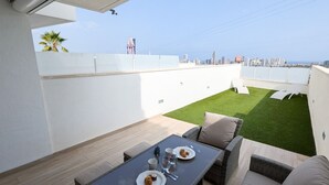 A rooftop terrace with a dining table, chairs, and a small lawn area. - PANORAMIC sweet home (Finestrat)