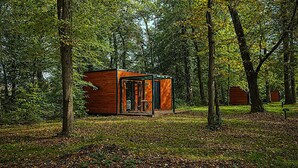 A small wooden cabin in a forest with a glass door and a table outside. - Hôtel Les Lodges De Vaugrigneuse (Vaugrigneuse)