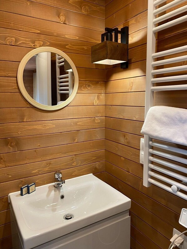 A bathroom with wooden paneling, a round mirror, a white sink, and a towel rack.