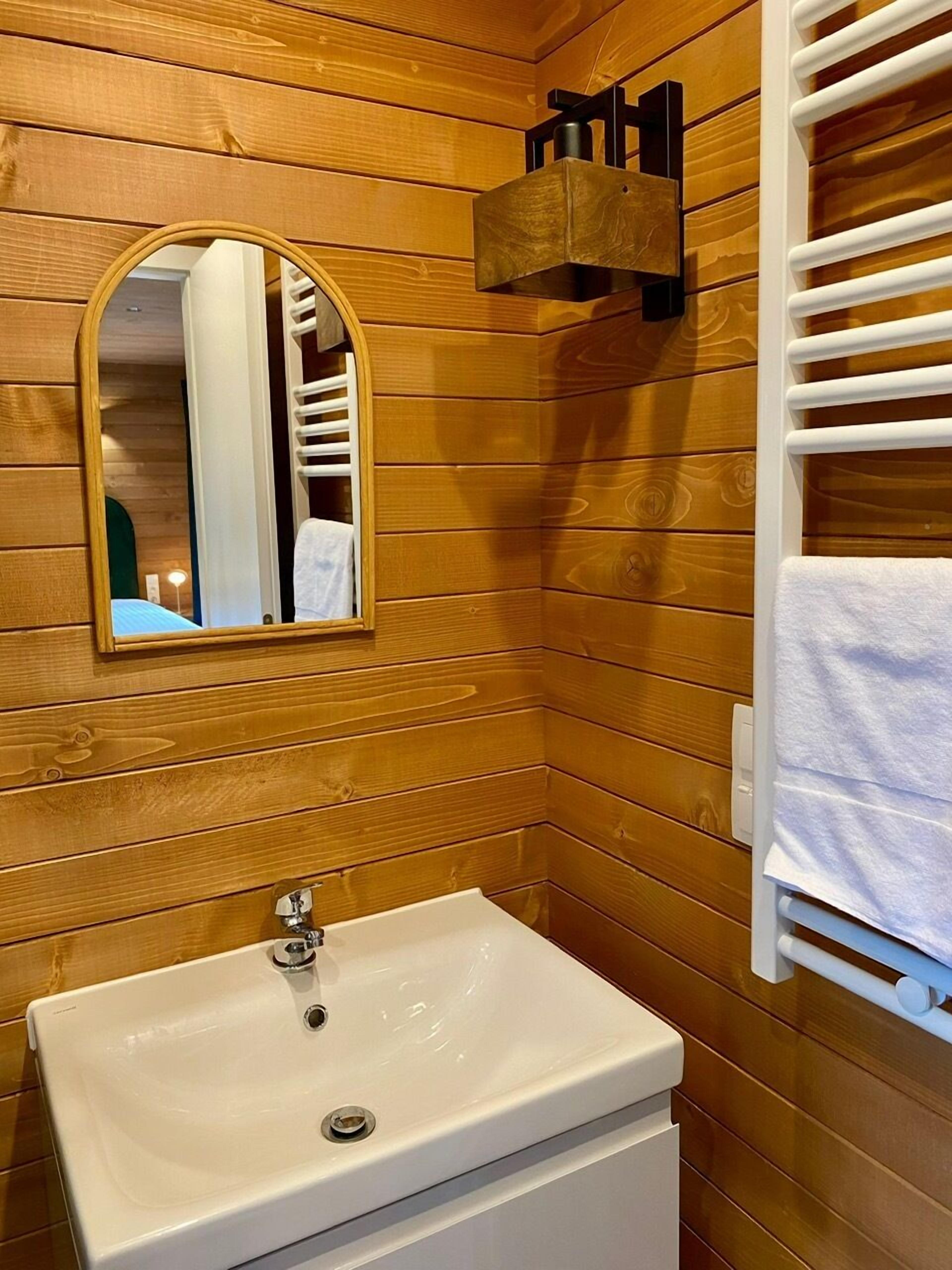 Une salle de bain avec des murs recouverts de lambris en bois, un lavabo blanc, un miroir et un porte-serviettes.