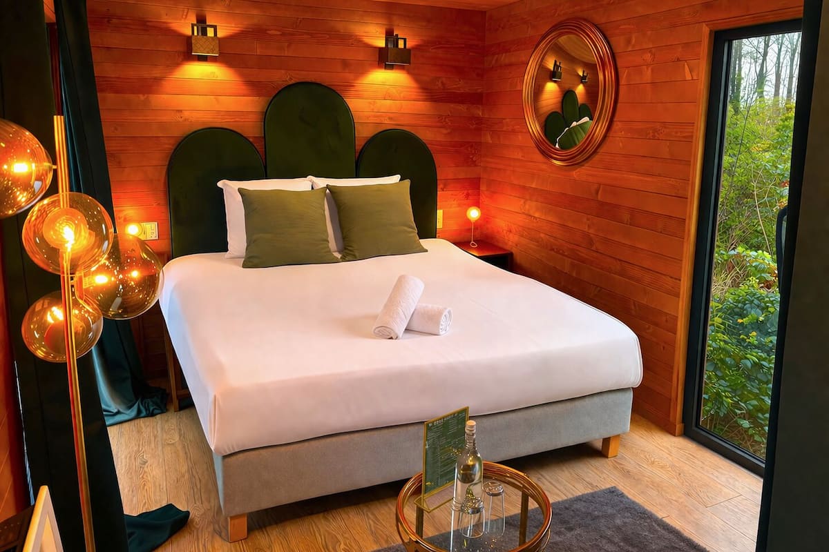 A modern bedroom with a large bed, wooden walls, and a view of greenery.
