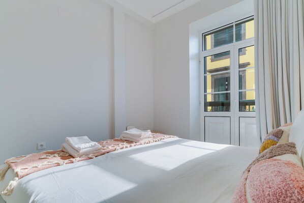 A bedroom with a bed, a window with curtains, and a view of buildings outside. - Funchal City Nest II (Funchal)