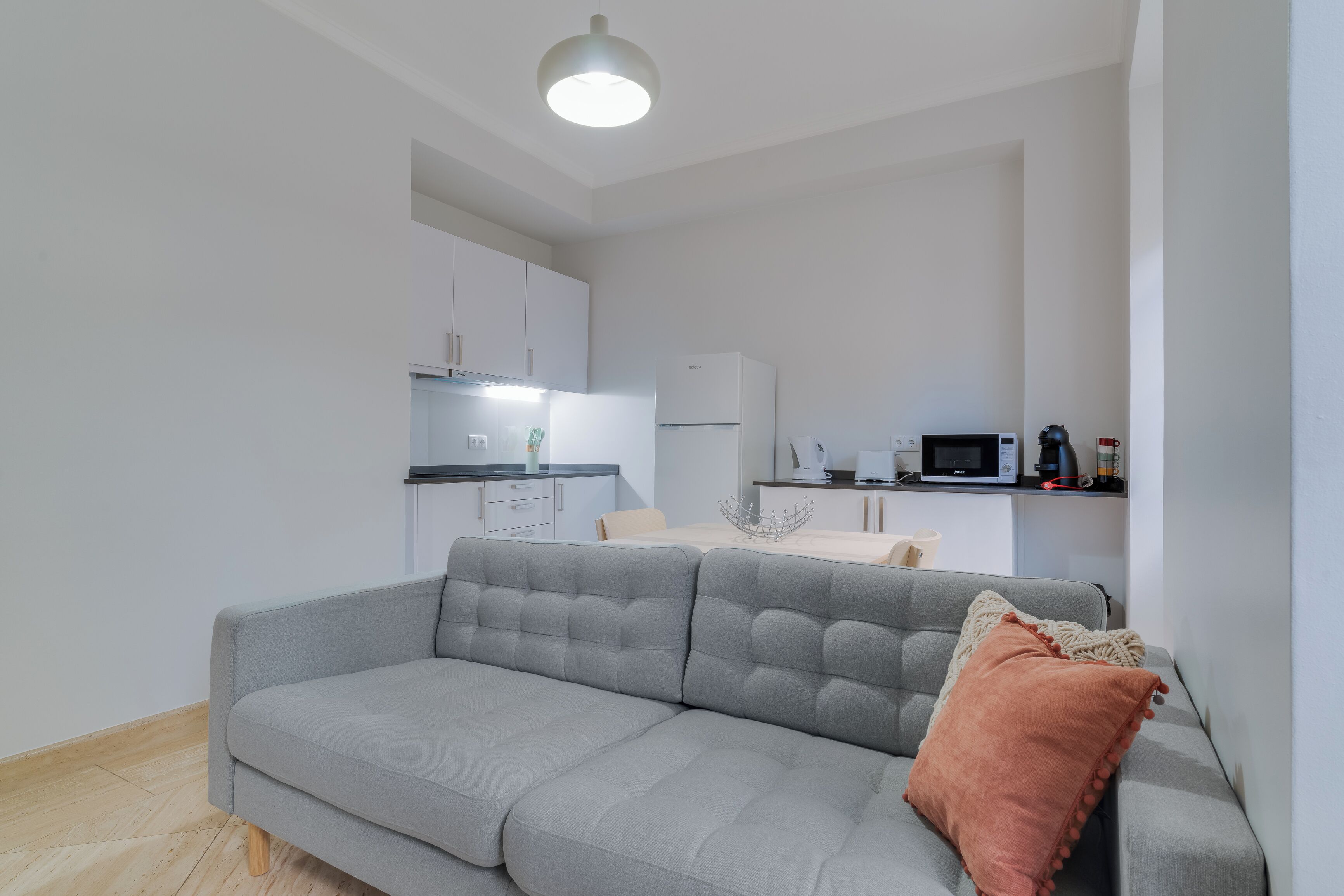 Een moderne woonkamer met een grijze bank en een keuken op de achtergrond.