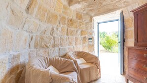 A stone-walled room with two cushioned seating areas, a wooden cabinet, and a door leading outside. - 4010 Tenuta I Trulli Rochira by Barbarhouse (Ceglie Messapica)