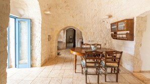 A stone-walled dining area with a round wooden table and chairs, an arched doorway, and a cabinet with glass doors. - 4010 Tenuta I Trulli Rochira by Barbarhouse (Ceglie Messapica)