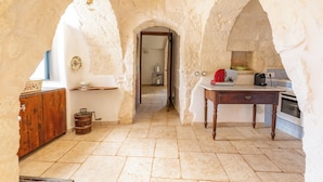 A rustic kitchen with stone walls, a wooden cabinet, a tiled floor, and a small table. - 4010 Tenuta I Trulli Rochira by Barbarhouse (Ceglie Messapica)