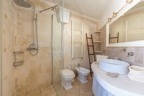 Et badeværelse med bruseniche i glas, toilet, bidet og en stor vask med et spejl over.