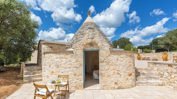 A stone building with a conical roof, a small door, and a table with chairs outside. - 4010 Tenuta I Trulli Rochira by Barbarhouse (Ceglie Messapica)