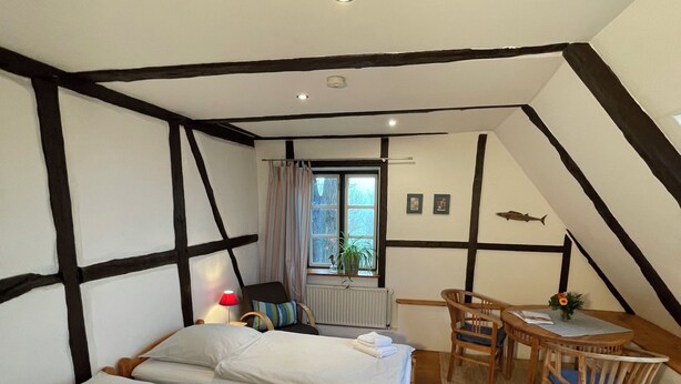 A room with two beds, a small table with chairs, a window with curtains, and a radiator. - Das Abendrote Haus (Suesel)