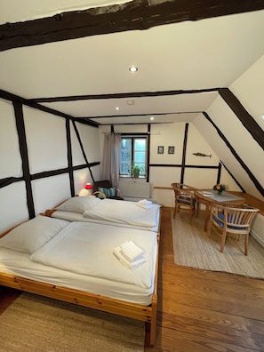 A room with two beds, a small table with chairs, a window with curtains, and a radiator. - Das Abendrote Haus (Suesel)