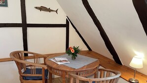 A cozy dining area with a round wooden table and two chairs, a small vase with flowers, and a fish decoration on the wall. - Das Abendrote Haus (Suesel)