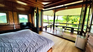 A room with a bed, a television, and a balcony with a table and chairs. - Natura Ravee Greenstay (Mae Taeng)