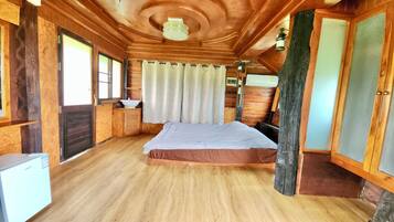 Een houten slaapkamer met een bed, een klein wastafeltje en een raam met gordijnen.