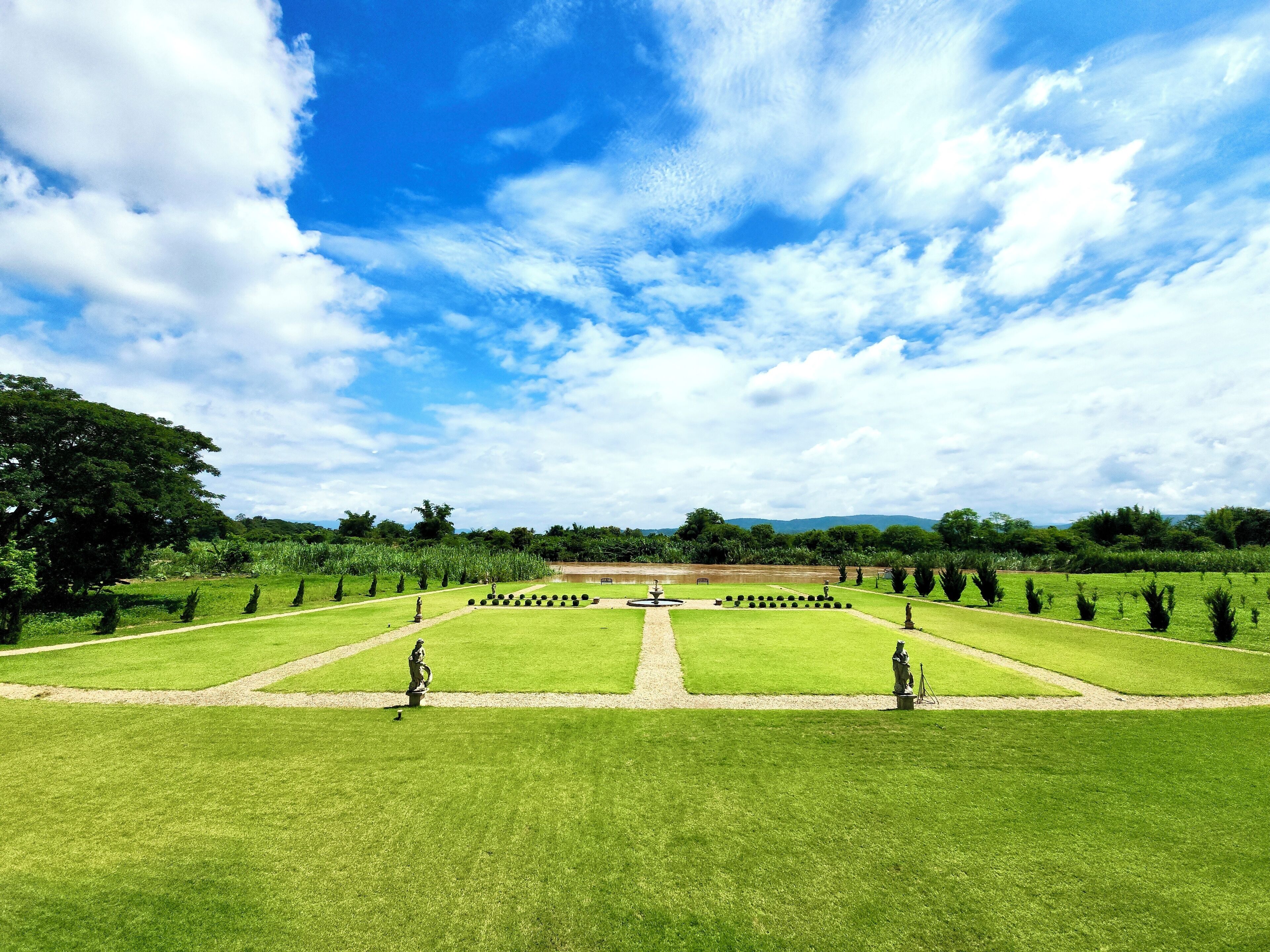 A well-maintained garden with a central fountain, surrounded by neatly trimmed hedges and trees.