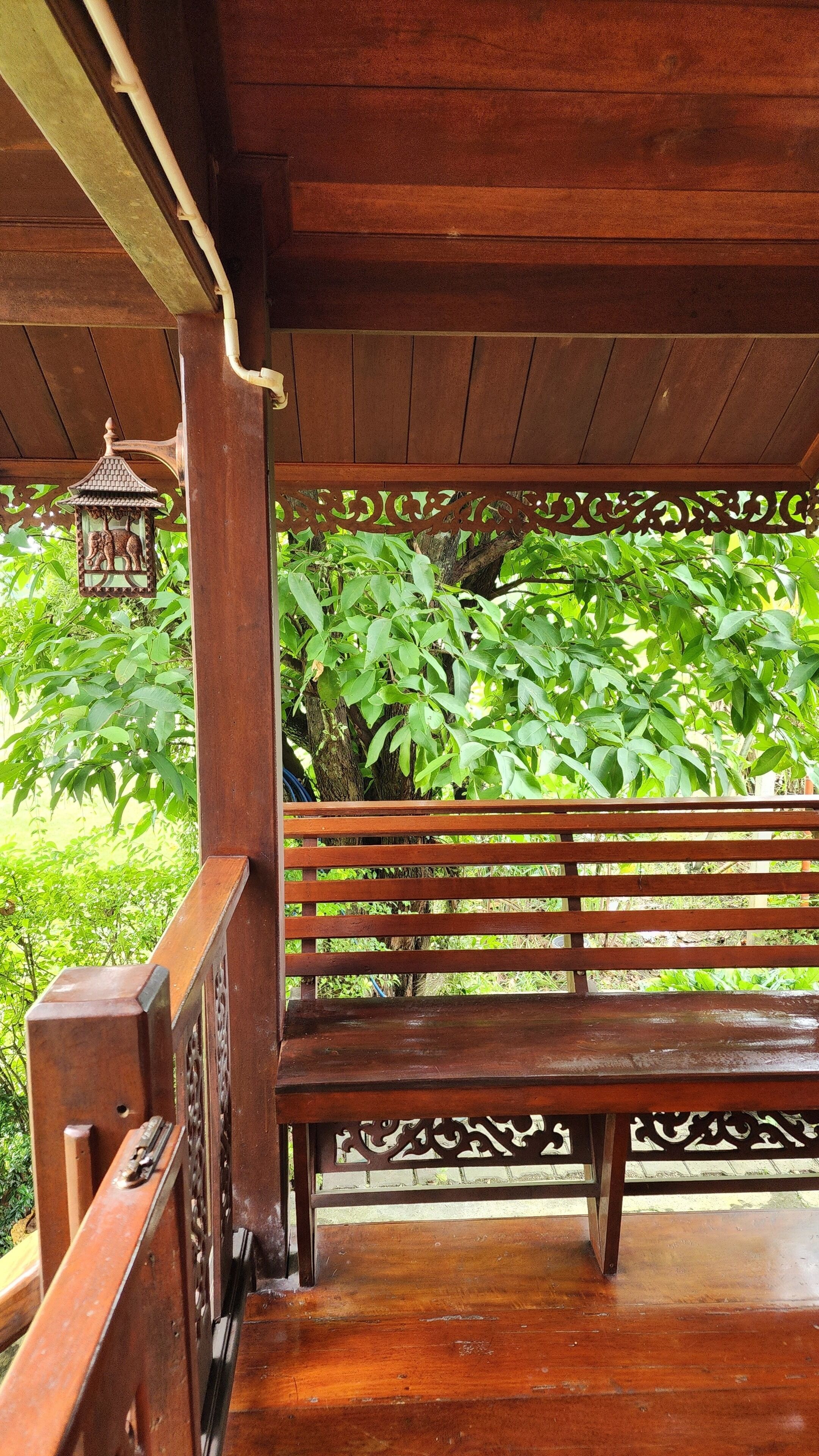 A wooden bench under a covered area with a decorative railing and a hanging lantern.