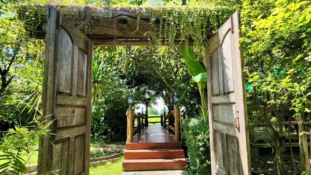 A wooden archway leading to a pathway surrounded by lush greenery. - Natura Ravee Greenstay (Mae Taeng)