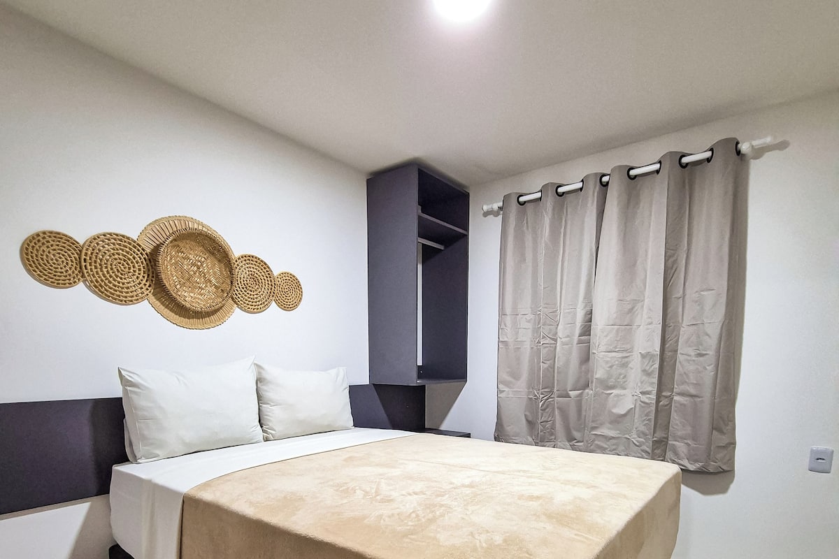 A bedroom with a bed, a headboard, a wall-mounted shelf, a curtain, and a ceiling light.