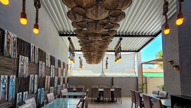 A restaurant with a long counter, multiple tables, and chairs. There are hanging baskets and lights on the ceiling. - Pousada Naala (Ipojuca)
