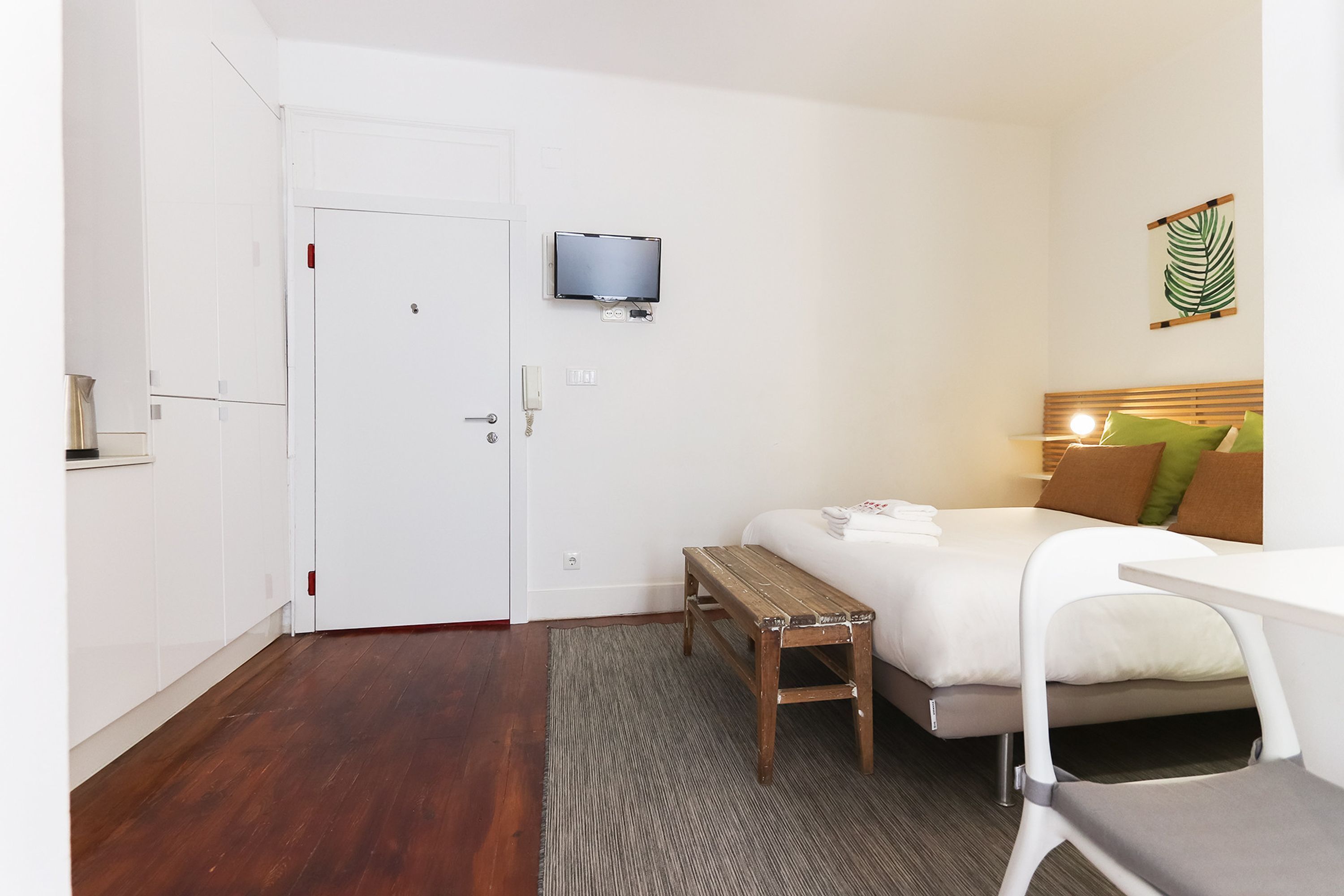 Une chambre d’hôtel avec un lit, un bureau, un téléviseur fixé au mur et une porte.
