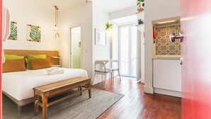 A hotel room with a wooden bed, a bench, a desk, and a kitchenette. - Santos Tiny Studio II by Homing (Lisbon)