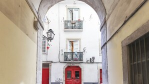 A narrow alleyway with a red door at the end, a motorcycle parked to the side, and a white building with balconies and windows. - Santos Tiny Studio II by Homing (Lisbon)
