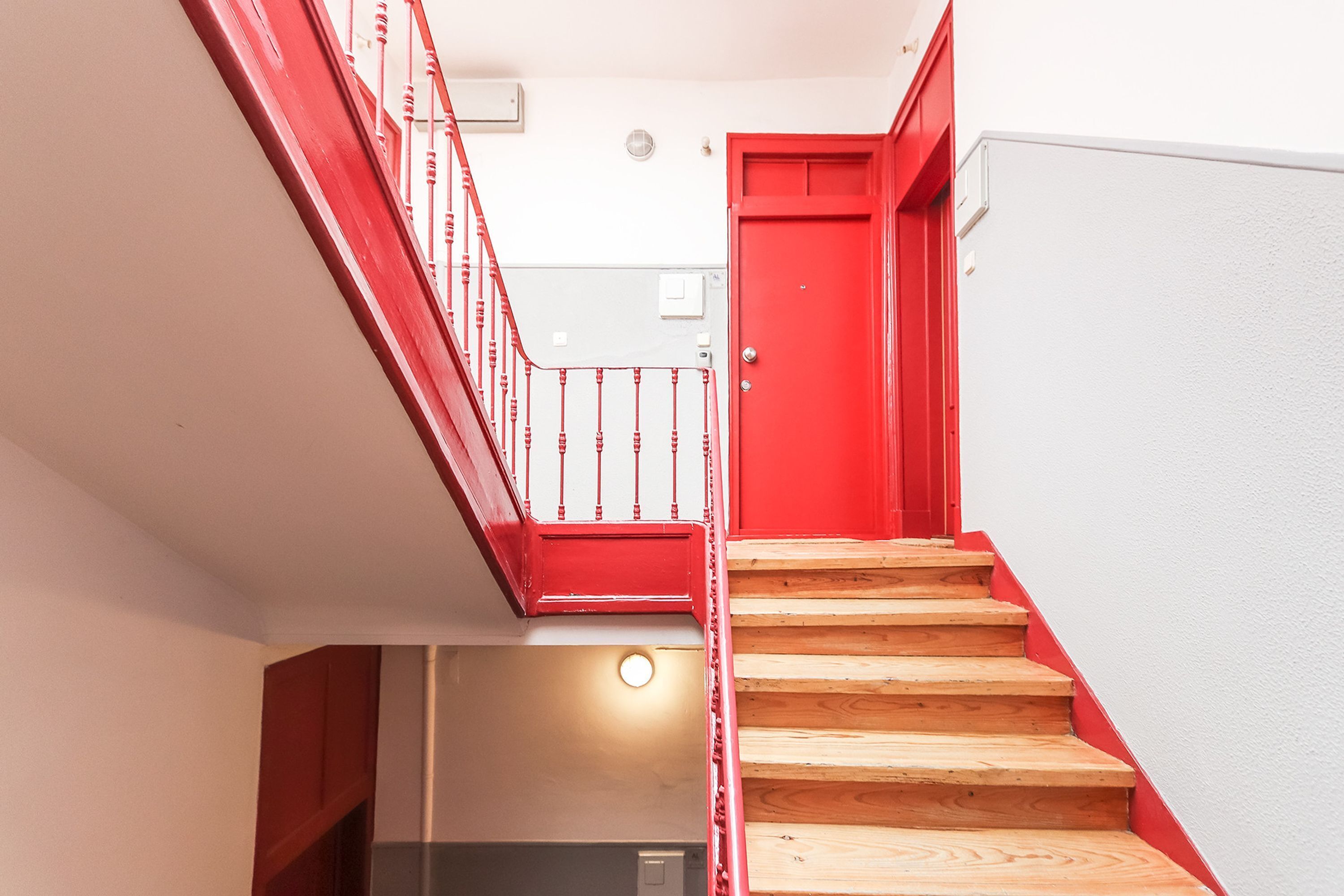 Una escalera de madera con barandilla roja que lleva a una puerta roja.
