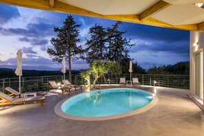 Une piscine sur le toit, agrémentée de chaises longues et de parasols, entourée d’arbres et offrant une vue panoramique.