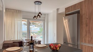 A modern kitchen with a stainless steel refrigerator, a dining area with a table set for two, and a view of the outdoors. - AeNaos Luxury Villa (Chania)