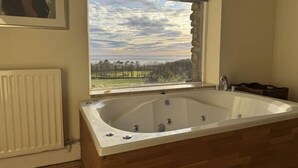 Une salle de bain avec une grande baignoire, une fenêtre donnant sur les arbres et le ciel, et un radiateur.