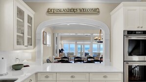 A kitchen with white cabinetry, a double oven, and a view of the ocean through large windows. - Oceanfront | 3 Decks, Walk to Grand Pavilion Pools & Boardwalk (Isle of Palms)