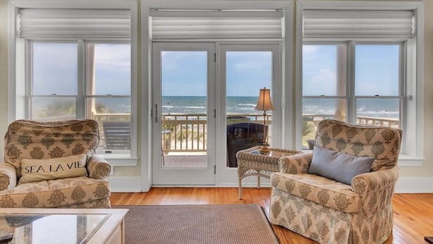 A room with two patterned armchairs facing a sliding glass door leading to a balcony with a view of the ocean. - Oceanfront | 3 Decks, Walk to Grand Pavilion Pools & Boardwalk (Isle of Palms)