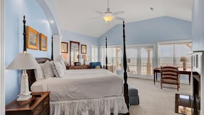 A bedroom with a four-poster bed, a ceiling fan, and a view of the outdoors through large windows. - Oceanfront | 3 Decks, Walk to Grand Pavilion Pools & Boardwalk (Isle of Palms)