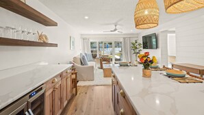 A modern kitchen with wooden cabinets, a central island, and a dining area with a sofa and chairs. - Kingston Arms Modern 1BR On Lido Key (Sarasota)