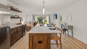 A modern kitchen with a central island, wooden cabinets, and a stainless steel refrigerator. - Kingston Arms Modern 1BR On Lido Key (Sarasota)