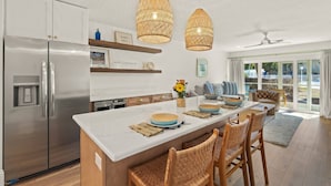 A modern kitchen with a central island, stainless steel appliances, wicker pendant lights, and a view to the outside. - Kingston Arms Modern 1BR On Lido Key (Sarasota)