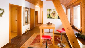 Interior de madeira com teto alto, mesa de jantar com duas cadeiras vermelhas e janela com vista para dentes-de-leão.