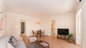 A modern living room with a sofa, coffee table, TV, dining area, and a staircase leading to another room. - Casa Telhados | Historic Center | Private Terrace (Faro)