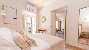 A bedroom with a large bed, a bedside table, a mirror, and a door leading to another room. - Casa Telhados | Historic Center | Private Terrace (Faro)
