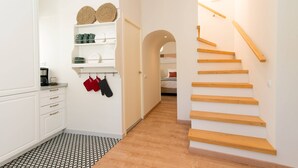 A modern kitchen with white cabinets, a patterned floor, and a wooden staircase leading to another room. - Casa Telhados | Historic Center | Private Terrace (Faro)