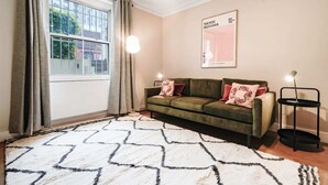 A living room with a green sofa, patterned rug, and a framed poster on the wall. - The Earl's Court Wonder - Adorable 1bdr Flat With Terrace (London)