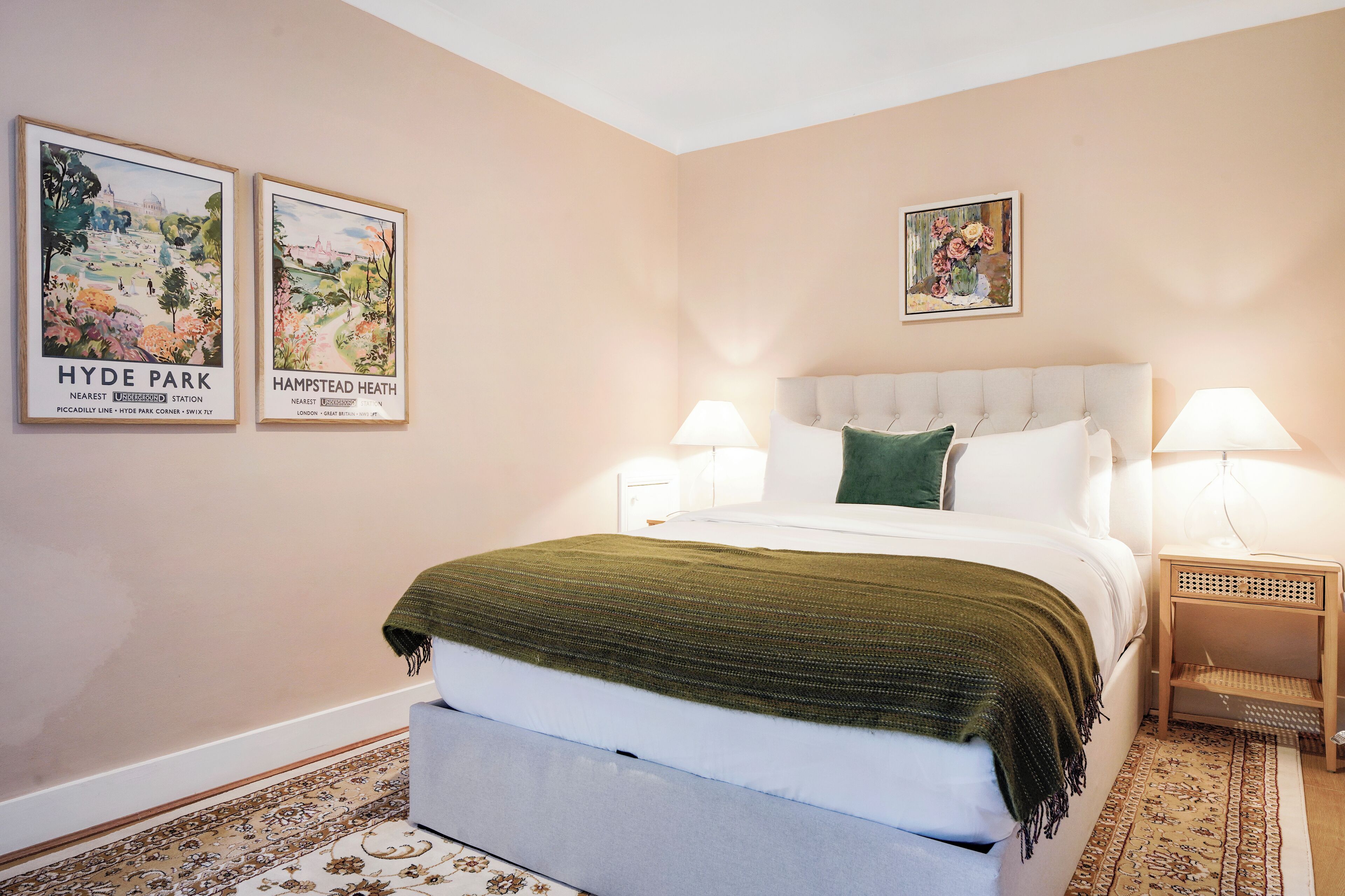 A bedroom with a large bed, two bedside tables with lamps, a green throw blanket, and two framed pictures on the wall.