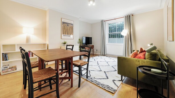 A modern living room with a wooden dining table, chairs, a sofa, a TV, and a bookshelf. - The Earl's Court Wonder - Adorable 1bdr Flat With Terrace (London)