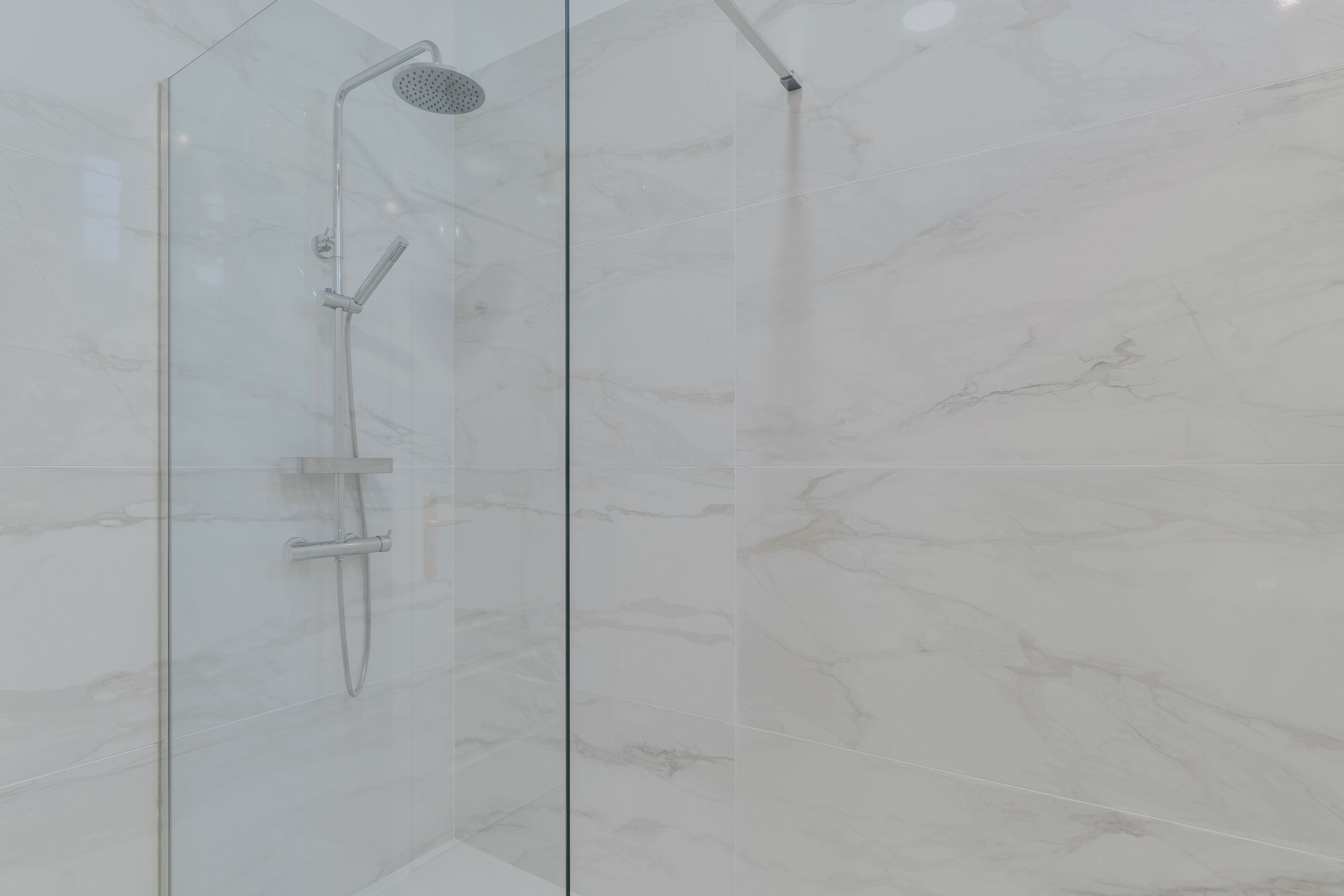 A glass-enclosed shower with a handheld showerhead and a wall-mounted faucet.