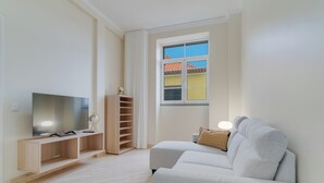 A modern living room with a flat-screen TV on a wooden stand, a sofa, and a window with a view of buildings. - Funchal City Nest III (Funchal)
