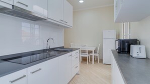 A modern kitchen with white cabinets, a black countertop, a sink, a stove, a microwave, a toaster, and a dining table with chairs. - Funchal City Nest III (Funchal)