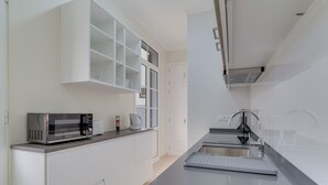 A modern kitchen with white cabinetry, a built-in microwave, a kettle, and a stainless steel sink. - Funchal City Nest III (Funchal)