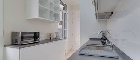 A modern kitchen with white cabinetry, a built-in microwave, a kettle, and a stainless steel sink.
