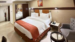Habitación de hotel con una cama grande, una mesita de noche con teléfono, una silla, una pequeña mesa y un espejo.